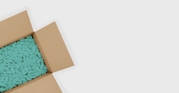On the right an open cardboard box with blue cornstarch packing pads and on the left an adhesive tape dispenser.